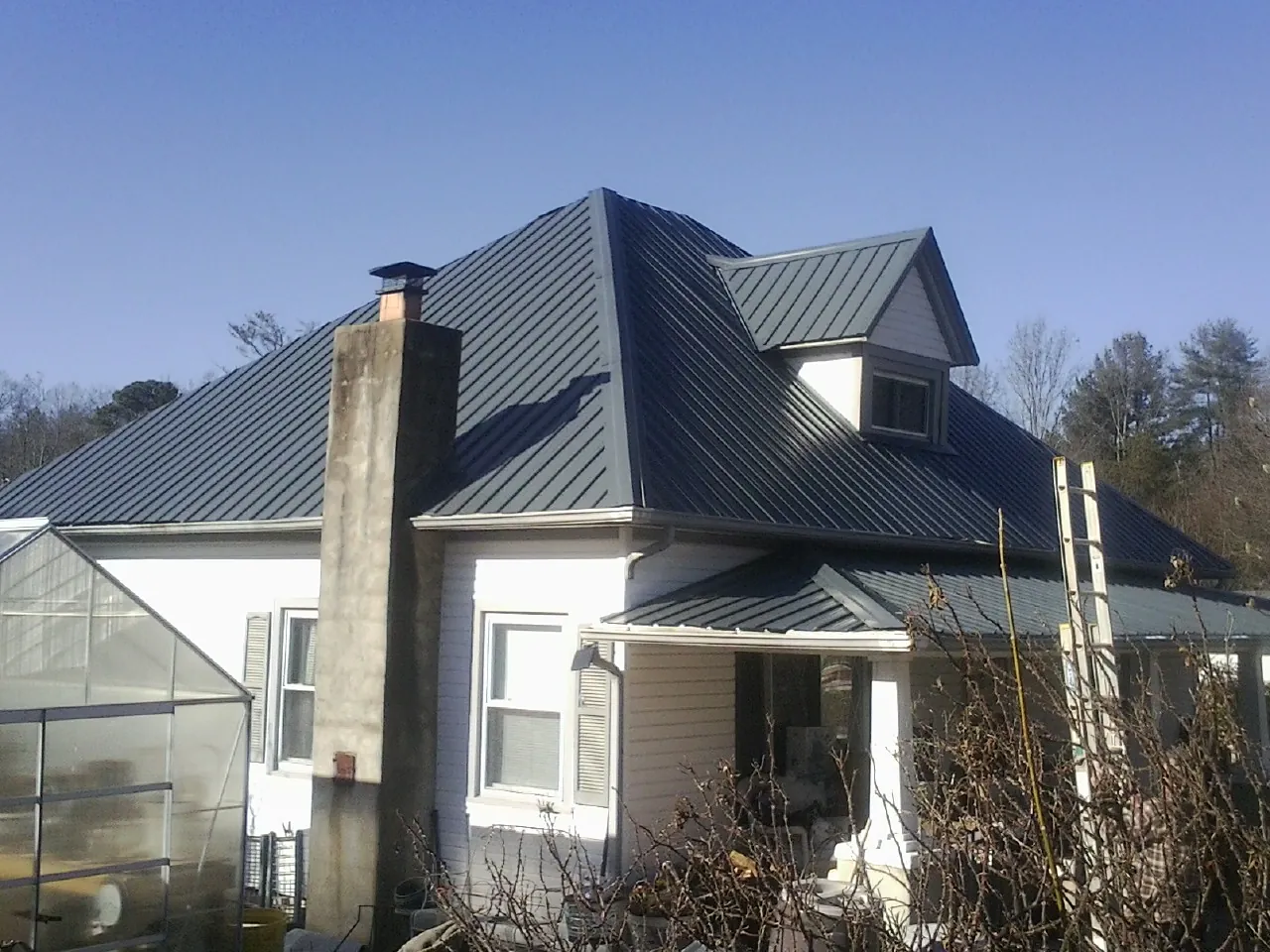 Dark blue standing seam metal roof on a white farmhouse with dormer — Slate & Tile Roof Repair by Roofing Brothers in Coralville