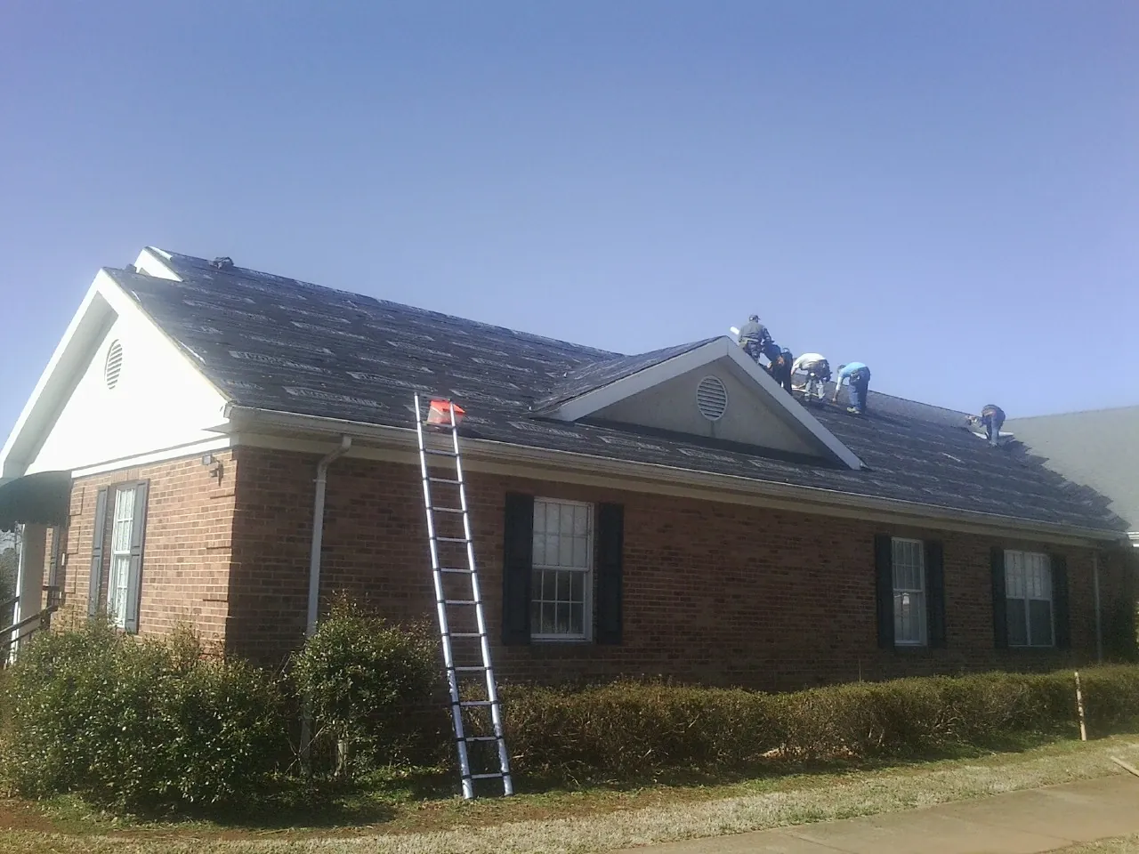 Crew tearing shingles off a brick ranch roof with a ladder set — Metal Roof Repair work by our crew in Coralville