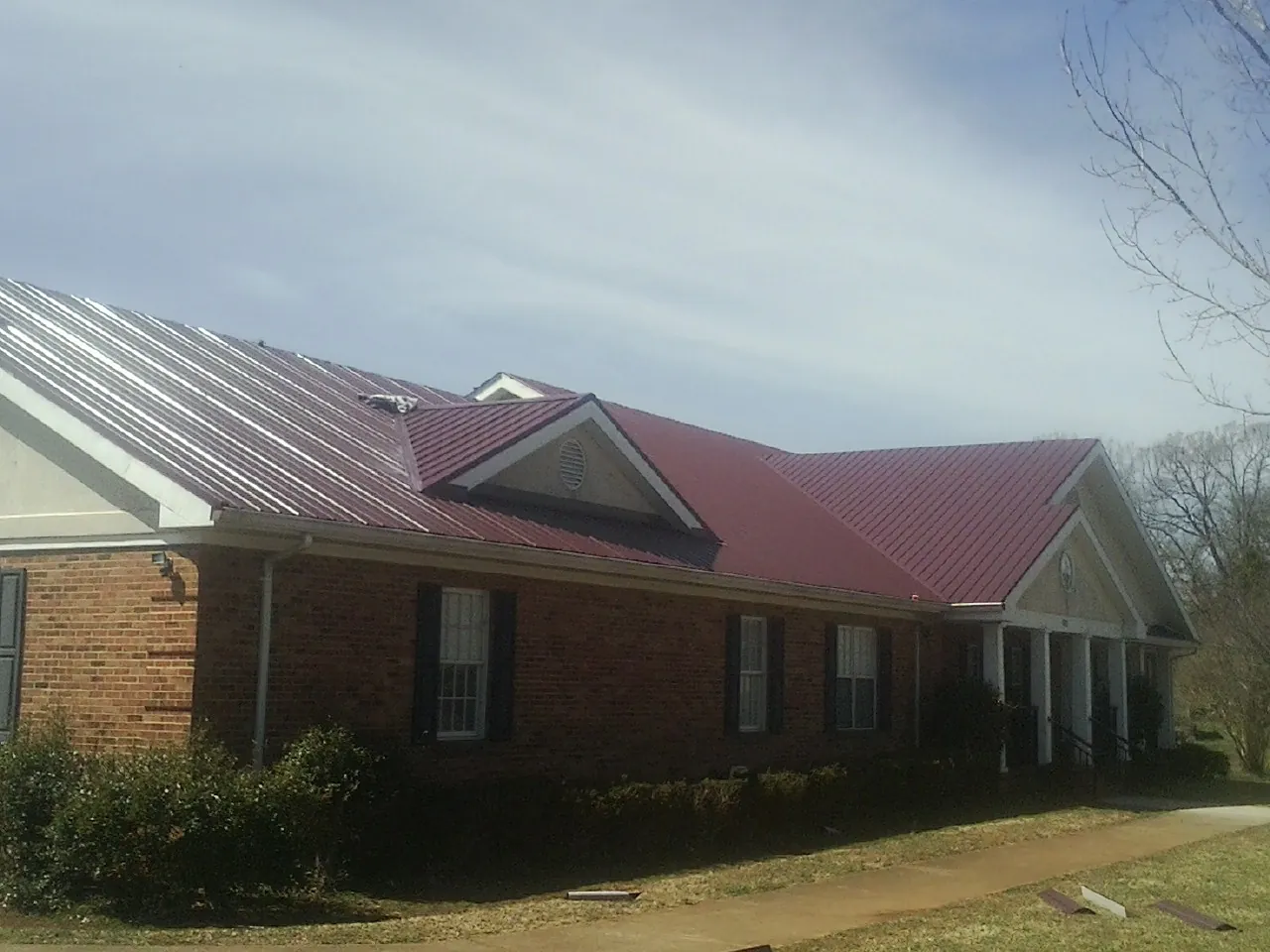 Red metal roof with gabled entries on a long brick building, from a Hail Damage Roof Repair job in Coralville