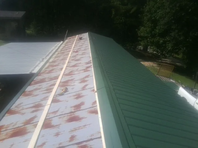 Old rusted panels beside newly installed green metal roofing — Wind Damage Roof Repair by Roofing Brothers in Coralville