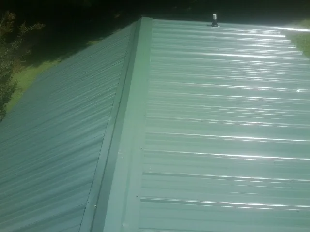 New green metal panels meeting at the ridge of a roof — Flat Roof Repair work by our crew in Coralville