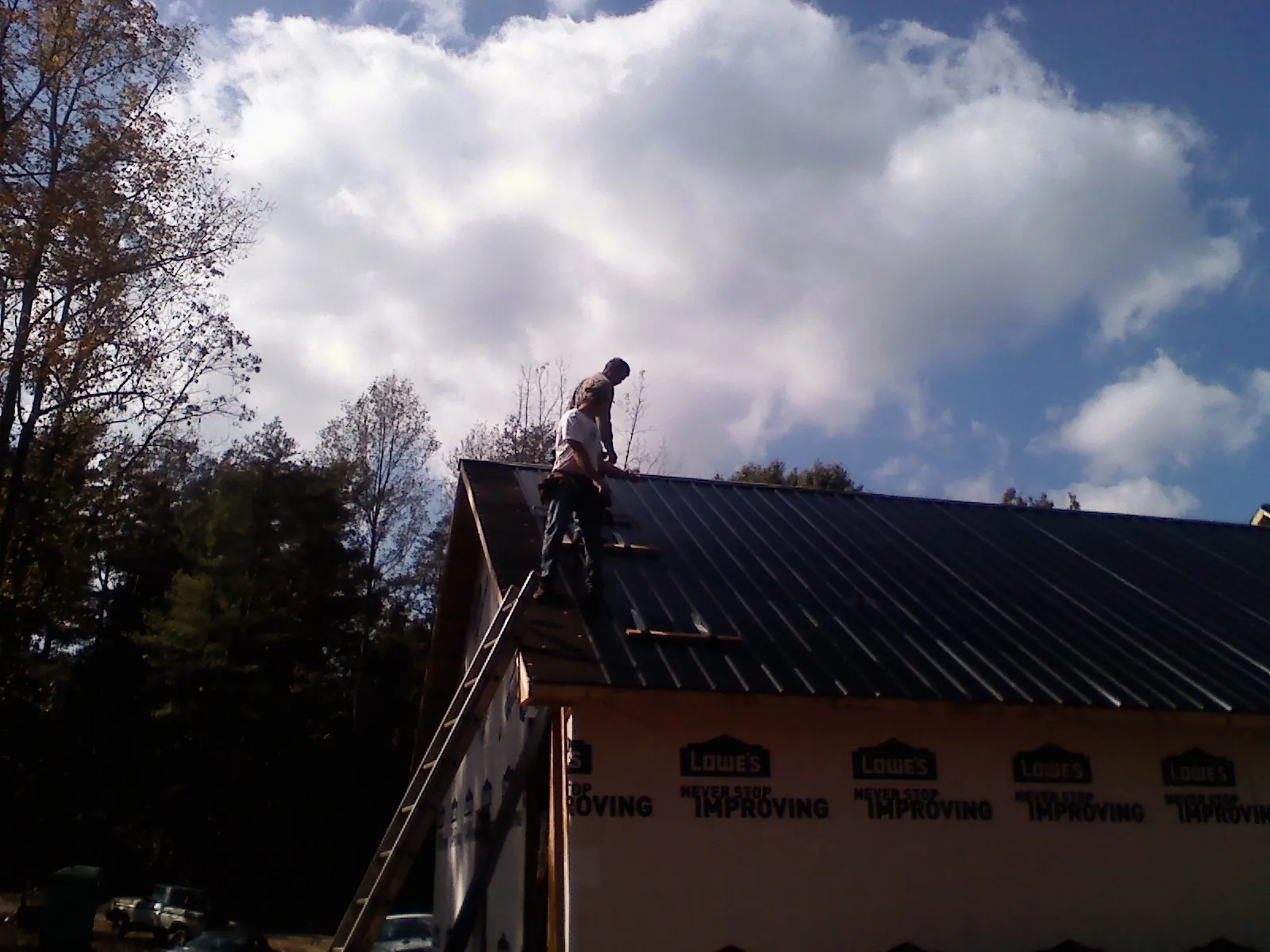 Roofer fastening dark metal panels high against a cloudy sky, from a Roof Inspection job in Coralville