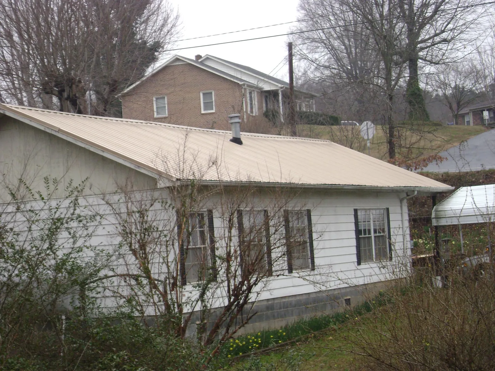 Tan metal roof on a white sided house set into a hillside — Commercial Roofing by Roofing Brothers in Coralville