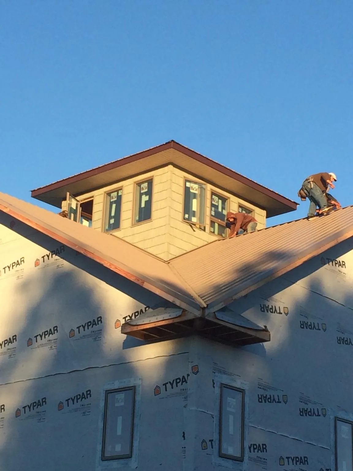 Roofers working around a rooftop cupola on a new metal roof at sunset — Roof Waterproofing in Coralville by Roofing Brothers